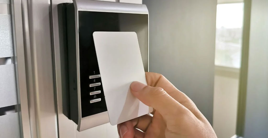 Main tenant un badge RFID blanc devant un lecteur électronique avec voyant vert indiquant l'accès autorisé
